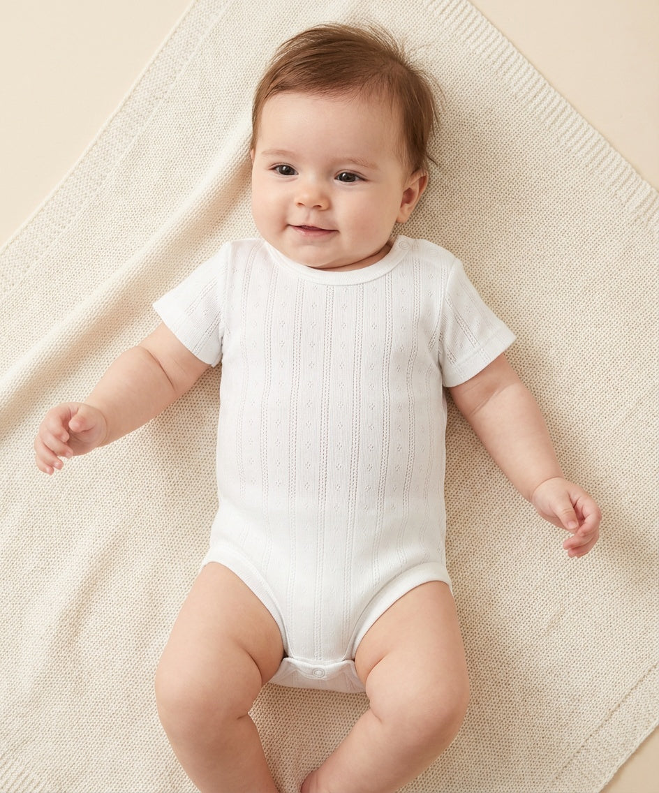 Baby wearing an organic white bodysuit lying on a textured beige surface

